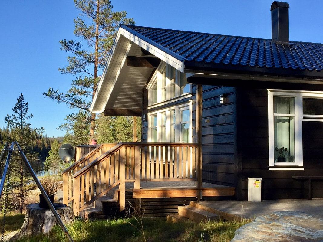 Mørk hytte med terrasse og stor glassvegg i skogen