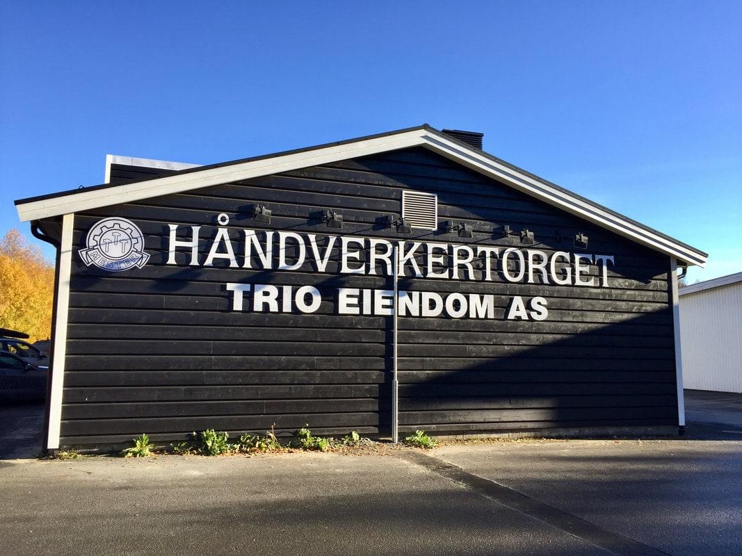 Håndverkertorget: et mørkt næringsbygg med skilt for Trio Eiendom AS